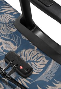 Kova matkalaukku, jossa on sininen kangaspinta ja beige lehtikuvio. Sisältää mustan lukitusmekanismin ja tukevan vetokahvan.