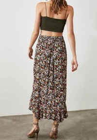 Maxi skirt with a dark floral pattern, featuring an elastic waistband and a ruffled hem. Paired with a fitted olive green crop top.