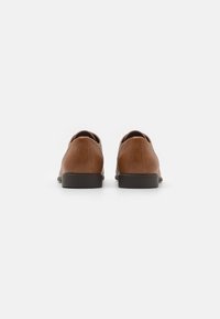 Brown leather shoes with a smooth texture, rounded toe, and low black rubber heel; minimalistic design and clean lines on the back.