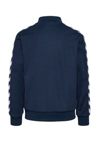 Felpa navy con colletto alto, caratterizzata da strisce diagonali bianche sulle maniche, polsini e orlo a costine, e una trama di tessuto liscia.