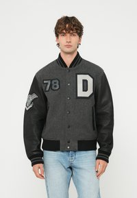 Šedá univerzitná bunda z vlnenej zmesi s čiernymi koženými rukávmi, rebrovaným golierom a elastickými manžetami. Na hrudi má nášivky "78" a "D".