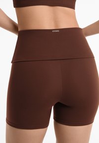 Brown high-waisted shorts made from smooth, stretchy material with a fold-over waistband, featuring the "OYSHO" logo at the back.