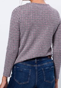 Mujer con una blusa de manga larga de patrón de pata de gallo metida en unos vaqueros oscuros con bolsillos traseros, vista desde la parte de atrás.