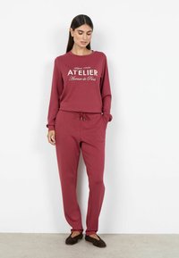 Bordowy zestaw do noszenia w domu składający się z długiego topu z nadrukiem "ATELIER" w białym kolorze oraz dopasowanych spodni ze sznurkiem; miękki, teksturowany materiał.