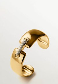 Pulsera de puño de oro con un acabado pulido suave conectada por una barra curva engastada con pequeños diamantes brillantes.