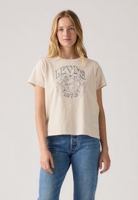 Lys beige kortermet t-skjorte med grafisk trykk av en ørn og "Levi's 1873" tekst i marineblått på en glatt bomullsstoff.