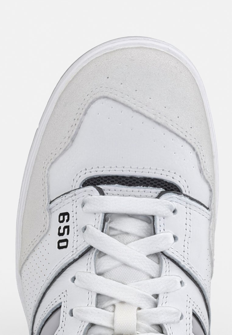 Weißer Sneaker mit Obermaterial aus Leder und Wildleder, Netz-Zunge und kontrastierenden schwarzen Akzenten. Mit eingeprägter Nummer 650 in der Nähe der Schnürsenkel.