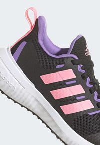 Sneakers sportivi neri con materiale in rete, dettagli rosa e viola, suola bianca e un prominente design a tre strisce sui lati.