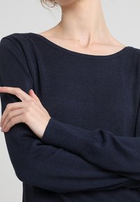 Navy blue, knitted sweater with a wide boat neckline. Long sleeves feature ribbed cuffs. Soft texture, form-fitting design.