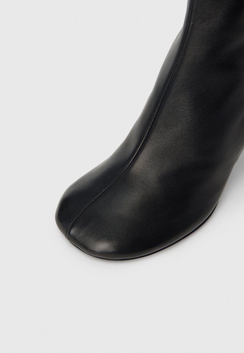 Bottine en cuir noir avec bout arrondi, texture lisse et design minimaliste. Présente une silhouette élégante sans aucune quincaillerie visible.