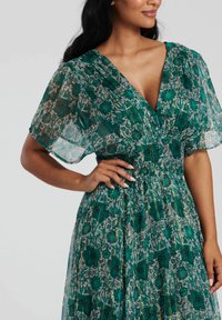 Robe fleurie verte en tissu léger et transparent avec un décolleté en V profond, des manches courtes et des détails imprimés. Dotée d'une taille cintrée.