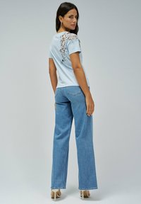 Camiseta azul claro con detalles de encaje en el hombro, combinada con Jeans de pierna recta de talle alto. Tejido suave, corte relajado y textura suave.