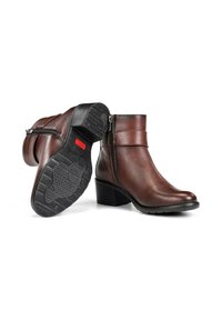 Botas de tobillo de cuero marrón con cremallera lateral, tacón apilado, suela de goma negra texturizada y detalle de correa minimalista en la parte superior.