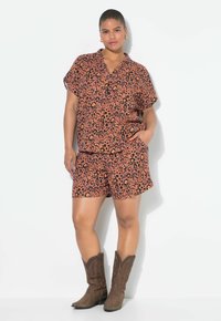 Leopardprint t-shirt met korte mouwen en bijpassende shorts in oranje en zwarte stof, met een relaxte pasvorm. Bruine cowboylaarzen maken de look compleet.