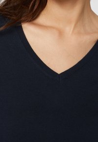 Maglione a maglia color navy con scollo a V e collo a coste. Il materiale sembra morbido con una consistenza liscia e un motivo uniforme.
