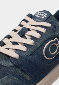 Μπλε τζιν αθλητικό παπούτσι με λευκά κορδόνια, μεγάλο λογότυπο "C" στο πλάι και ετικέτα με την επιγραφή "Coach" στη γλώσσα.