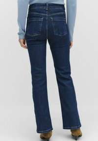 Tummansininen farkkukangasta valmistetut leveälahkeiset farkut, joissa on korkea vyötärö, takataskut ja siisti helma. Materiaali näyttää olevan kestävä ja sileä tekstuuriltaan.