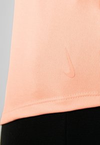 Camiseta deportiva de color melocotón con diseño acanalado y un logo de Nike en tono a juego, con dobladillo recto y tejido texturizado, combinada con leggings negros.
