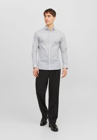 Camicia abbottonata grigia chiara con un piccolo motivo, maniche lunghe e colletto, abbinata a pantaloni neri e scarpe nere.