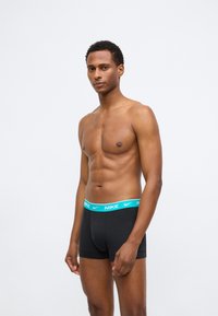 Boxer briefs noirs avec une ceinture en logo Nike turquoise, offrant une coupe ajustée et une texture lisse, présentés sur un modèle.