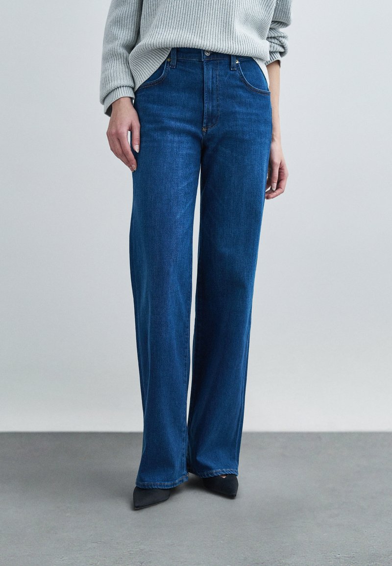 Μπλε τζιν παντελόνι με φαρδιά μπατζάκια από denim, με ψηλή μέση, μπροστινές τσέπες και κλασικό σχέδιο με πέντε τσέπες. Λείο ύφασμα με απαλή ξεθώριαση.