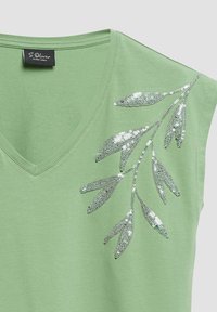 T-shirt vert clair à col en V avec manches courtes et motif feuille en sequins argentés sur l'épaule près de l'encolure et de la couture de la manche.