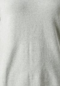 Maglione grigio chiaro, morbido e lavorato a maglia, caratterizzato da una texture liscia e un design semplice e privo di decorazioni, con una vestibilità rilassata.