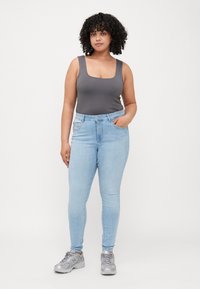 Bodysuit gris con escote en forma de scoop combinado con jeans skinny azul claro. La modelo lleva zapatillas deportivas plateadas. Textura suave en todo el conjunto.