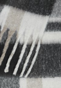 Rutete kasteteppe i grått, svart og beige ull. Har frynsete kanter og en myk tekstur med et fremtredende rutemønster.