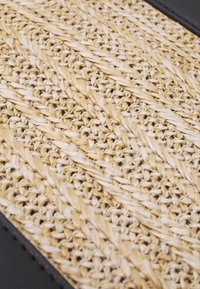 Pletený povrch z ratanu s texturovaným, přírodním vzorem v krémových a béžových tónech, lemovaný hladkým, tmavým okrajem.