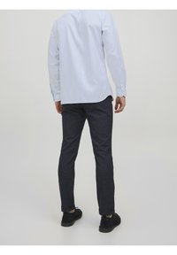 Světle modrá košile s dlouhým rukávem a knoflíkovými manžetami, spárovaná s tmavě modrými kalhotami na míru, které mají hladkou texturu a jemný vzor.