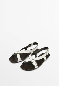 Black and white sandals with a cross-strap design, made of leather. Features an adjustable ankle strap and a flat, textured sole.