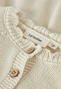 Maglione lavorato a maglia color crema con colletto arricciato, bottoni in legno e un'etichetta con la scritta "Lil' Atelier" di misura 1-2M. Tessuto strutturato.