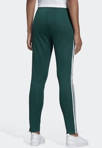 Zielone legginsy sportowe wykonane z miękkiego materiału, z białymi paskami po bokach i dopasowanym krojem, kończące się na kostce.