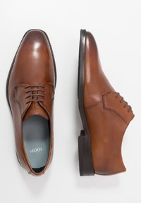 Chaussures habillées en cuir marron avec une finition lisse, design à lacets, bout rond et un petit talon empilé. L'intérieur est doublé de bleu clair.
