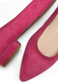 Bailarinas de ante rosa con punta afilada y un tacón bajo. Presentan una textura suave y un ribete elástico alrededor de la abertura.