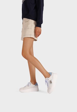 Sneakers platform bianchi con accenti azzurri, realizzati in materiale morbido, con punta rotonda e design con lacci. Mostrati dei pantaloni cargo beige corti.
