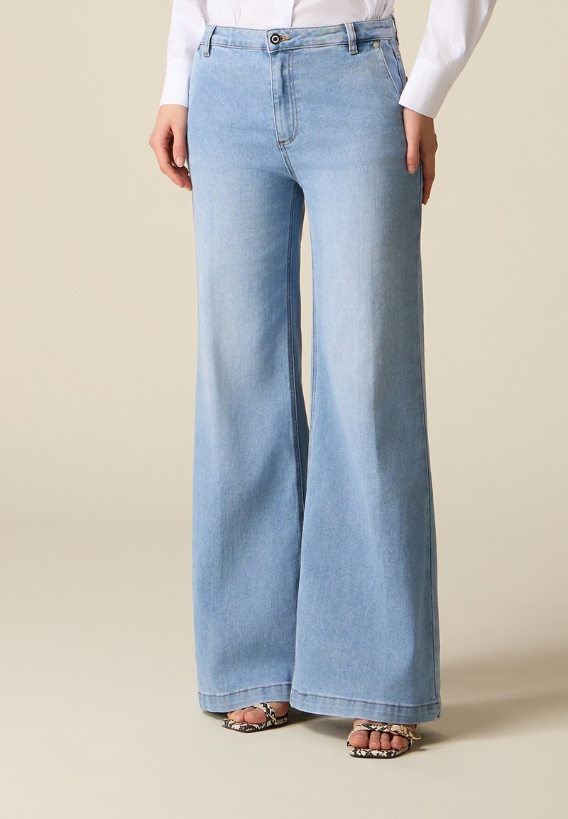 Blugi albastre deschis, cu picioare largi, purtați cu o cămașă albă, asortați cu sandale cu toc înalt, cu model de piele de șarpe și vârf decupat.