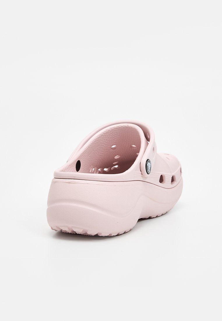 Zueco de goma rosa con agujeros de ventilación, forma redondeada y una correa trasera. Presenta un botón en el lateral. Textura suave y diseño ligero.