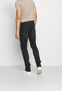 Svarta slim-fit jeans med en klassisk femfickdesign och subtila sömdetaljer. Bärs tillsammans med en ljusbeige T-shirt och vita sneakers.