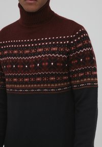 Strick-Turtleneck-Pullover mit einem burgunderfarbenen und mehrfarbigen gemusterten Einsatz, der in einen einfarbigen schwarzen Körper übergeht. Strukturierter Stoff.