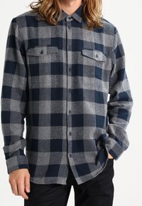 Marineblauwe en grijze geruite flanellen shirt met knoopsluiting, twee borstzakken en lange mouwen. Zachte textuur met een relaxed fit.