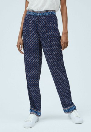 Hosen mit Navy-Muster, die einen dekorativen elastischen Bund mit kulturellen Motiven, gerade Beine und weiße Sneakers aufweisen.