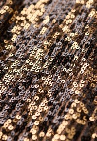 Materiał z cekinów z naprzemiennym wzorem czarnych i metalicznych złotych okrągłych cekinów, tworzący teksturowaną, błyszczącą powierzchnię.