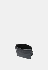 Borsa nera in pelle con chiusura a zip, caratterizzata da una texture liscia, forma rettangolare e una singola tracolla. All'interno sembra spaziosa.