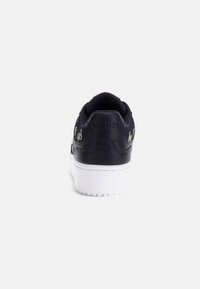 Black leather sneaker with a white rubber sole. Features logo on back, padded collar, and smooth texture. Classic low-top design.