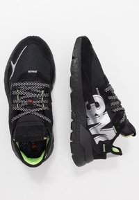 Zapatillas deportivas negras con materiales de malla y ante, que presentan una suela texturizada, acentos reflectantes y un distintivo branding de 3M.