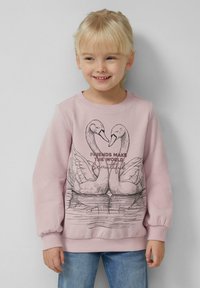 Noor tüdruk naeratab, seljas roosa sviiter, millel on kaks luike, kes moodustavad südame kujutise, koos tekstiga "Sõbrad muudavad maailma kauniks."