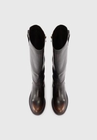 Bottes en cuir marron foncé, montantes, à bout arrondi, texture lisse et design asymétrique. Dotées de deux fermetures éclair sur le côté.