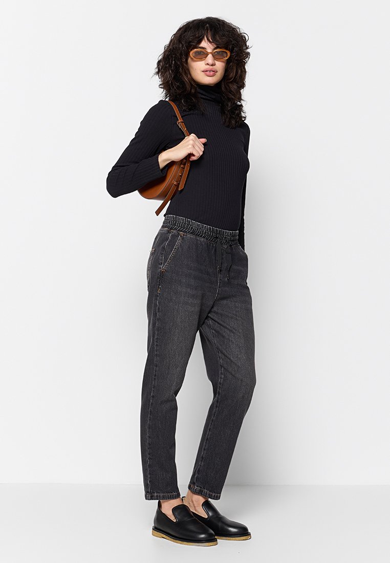 Maglione a collo alto nero a coste, jogger in denim grigio chiaro con vita elasticizzata e scarpe slip-on nere. Borsa a tracolla marrone e occhiali da sole arancioni.